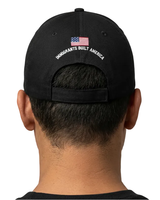 Black cap with 'Immigrants Built America' text and American flag on the back, worn by a person.