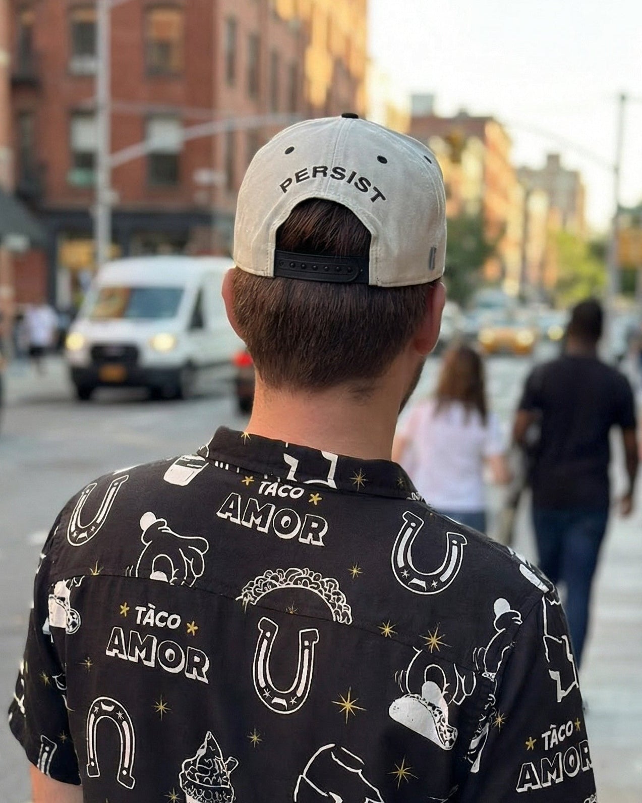 Person wearing a black shirt with white graphics and text, walking on a city street.