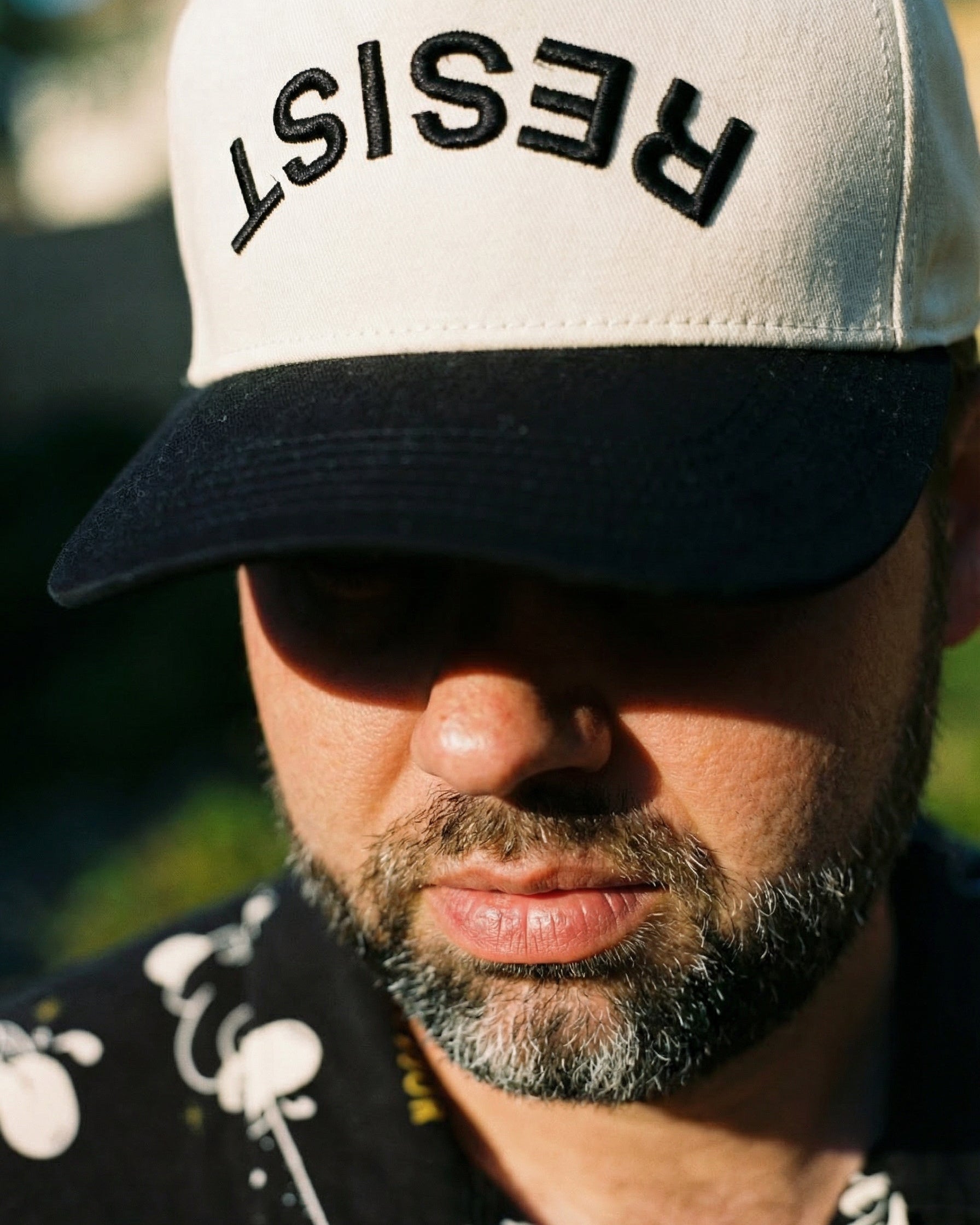 Person wearing a cap with 'RESIST' text in a blurred outdoor setting