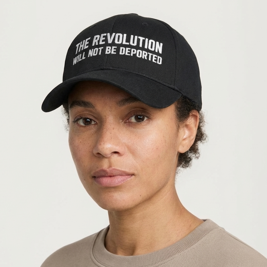 Person wearing a black cap with 'The Revolution Will Not Be Deported' text on a plain background